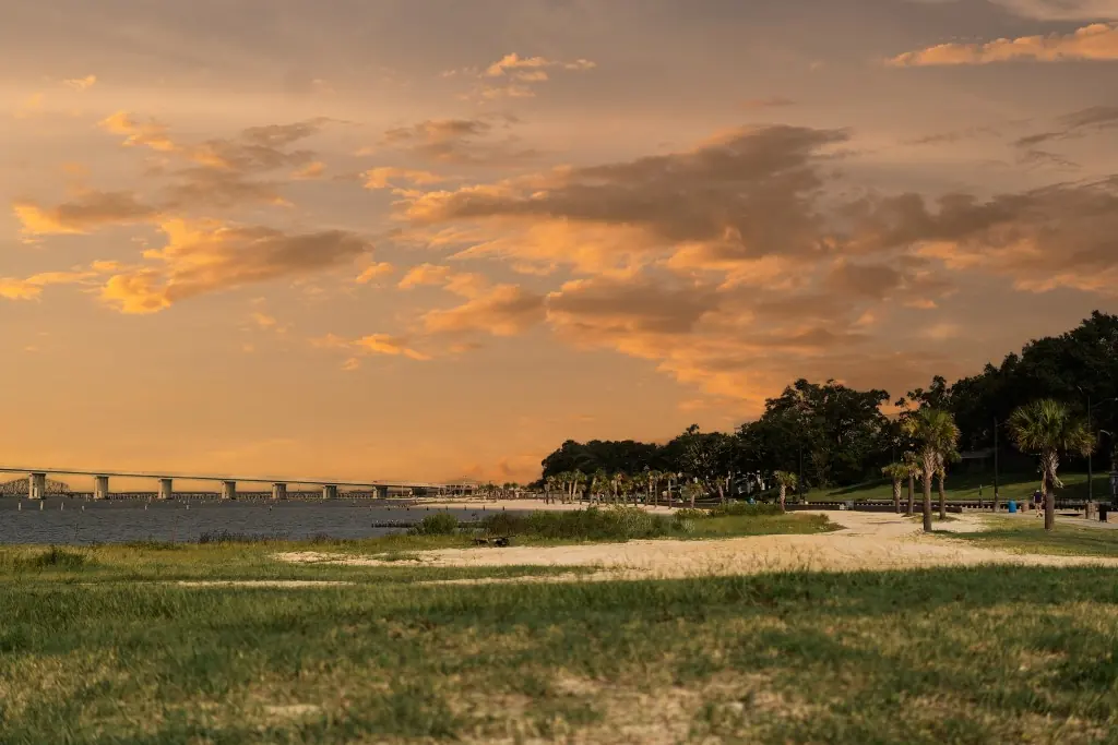 Sunset over a Gulf Coast shoreline with a sandy path, palms, and the Biloxi Bay Bridge near Ocean Springs, Mississippi